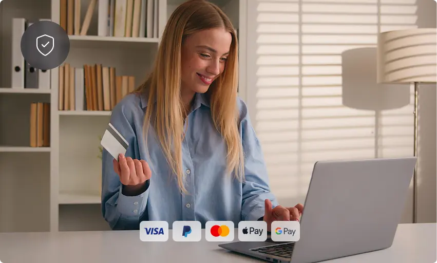 A woman sits at a desk holding a credit card and smiling at her laptop. On the screen are payment method icons for Visa, PayPal, Mastercard, Apple Pay, and Google Pay. A bookshelf and lamp are in the background.