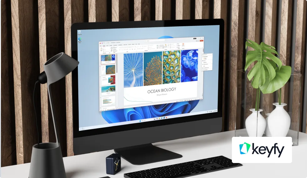 A computer on a modern white desk displays an Ocean Biology presentation. Nearby are a black lamp, a plant in a gray pot, a keyboard, a mouse, and a branded keyfy logo in the bottom right corner.