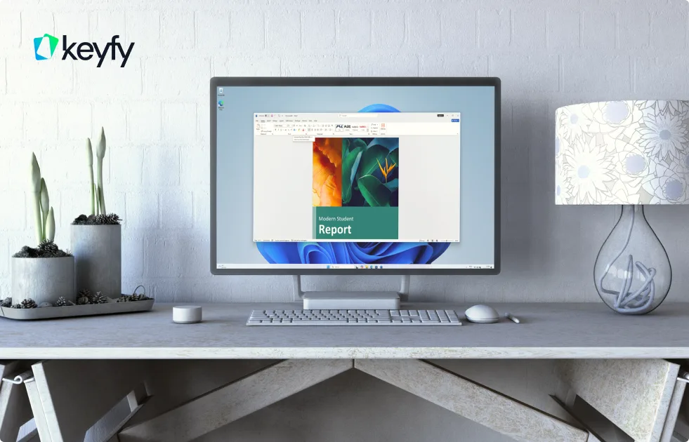 A desktop computer on a modern desk displays a report titled Student Report. The desk also holds potted plants, a keyboard, mouse, and a lamp. The Keyfy logo is visible in the top left corner.